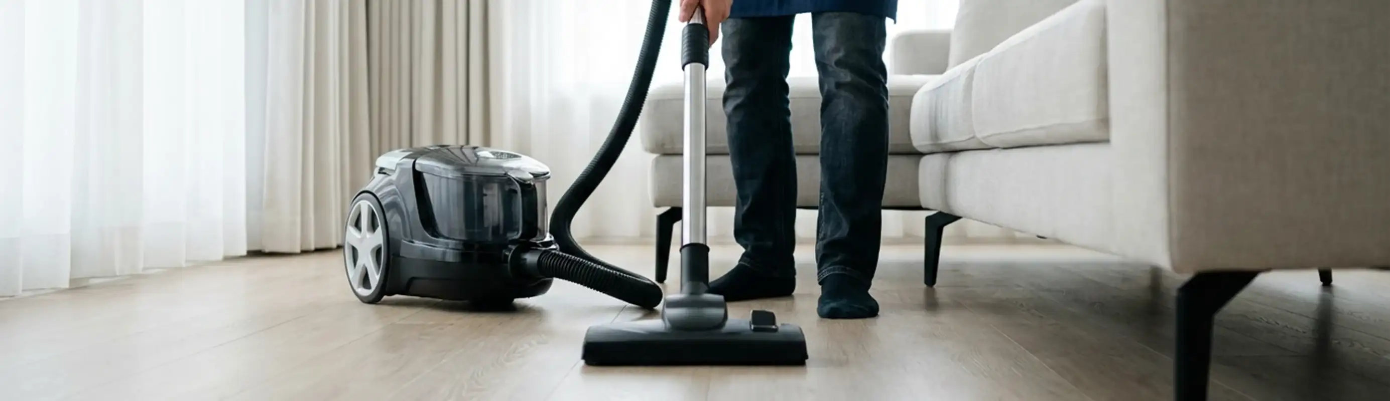 Professional house cleaner vacuuming a living room floor with a canister vacuum cleaner, Tuscaloosa, AL.