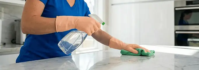 Maid service worker spraying and wiping a kitchen countertop with a microfiber cloth for sanitizing, Tuscaloosa, AL.