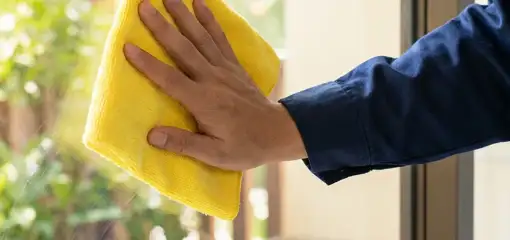 House cleaner wiping a glass window with a yellow microfiber cloth for streak-free cleaning, Tuscaloosa, AL.